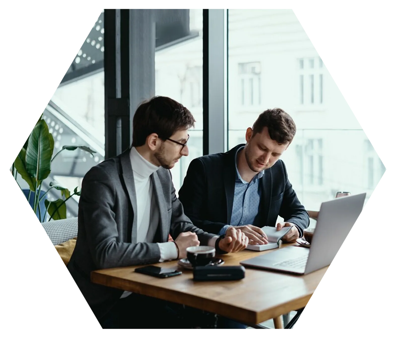 Two businessmen collaborate over documents and a laptop at a cafe, demonstrating important employability skills.