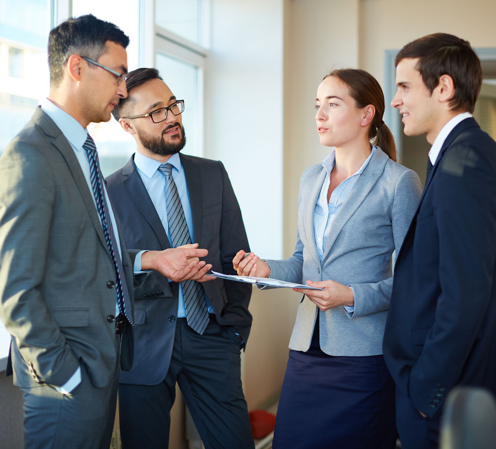 Four business professionals discuss documents and LLND standards in a modern office setting.