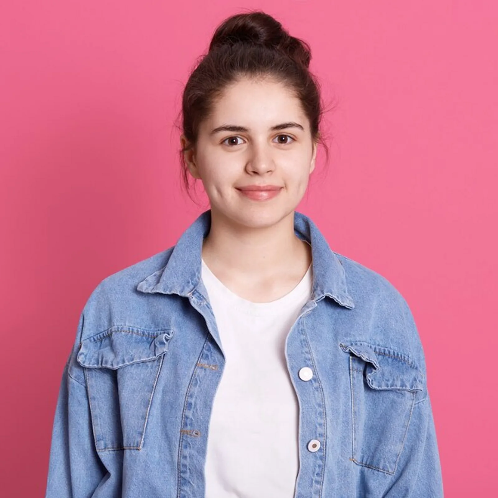 A young woman with brown hair wearing a denim jacket poses against a pink backdrop, representing skills development.